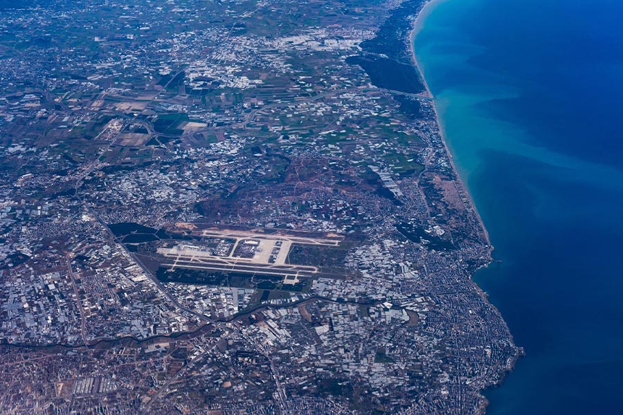 نمای هوایی از فرودگاه آنتالیا و نواحی اطراف آن در نزدیکی ساحل با آب‌های آبی و شفاف.