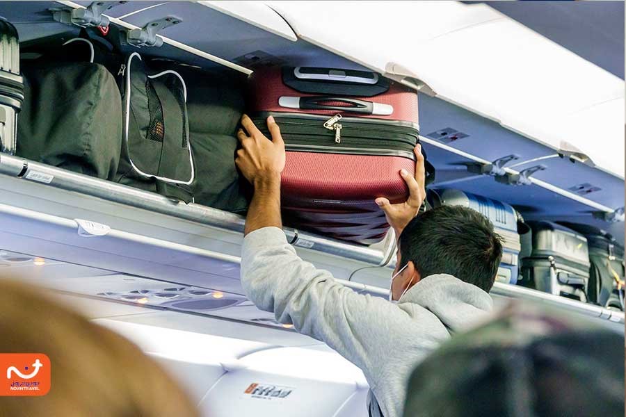 تصویری از مردی سوار هواپیما که در حال گذاشتن بار دستی خود در کابین مخصوص بارهای دستی است.