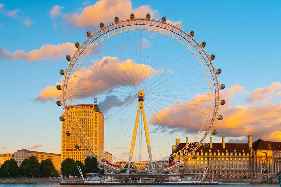 نمای کامل از چرخ و فلک چشم لندن با کابین‌های شیشه‌ای در برابر ابرهای رنگی آسمان